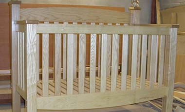 Front on angle of handmade baby cot, showing the delicate curving bottom and top lines