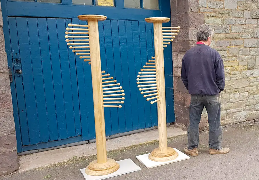Pair of handmade belt/scarf stands outside of workshop with man standing near for size comparison
